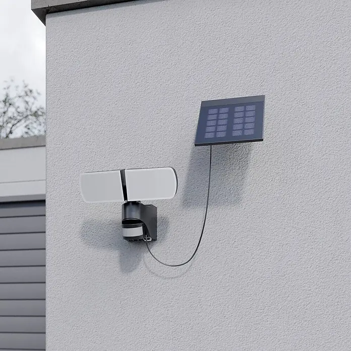 Arcchio Außenwandleuchte Lissano - schwarz, IP44 - Eine schwarze solarbetriebene Außenleuchte mit zwei weißen Lampen und separatem Solarpanel an einer strukturierten grauen Wand.
