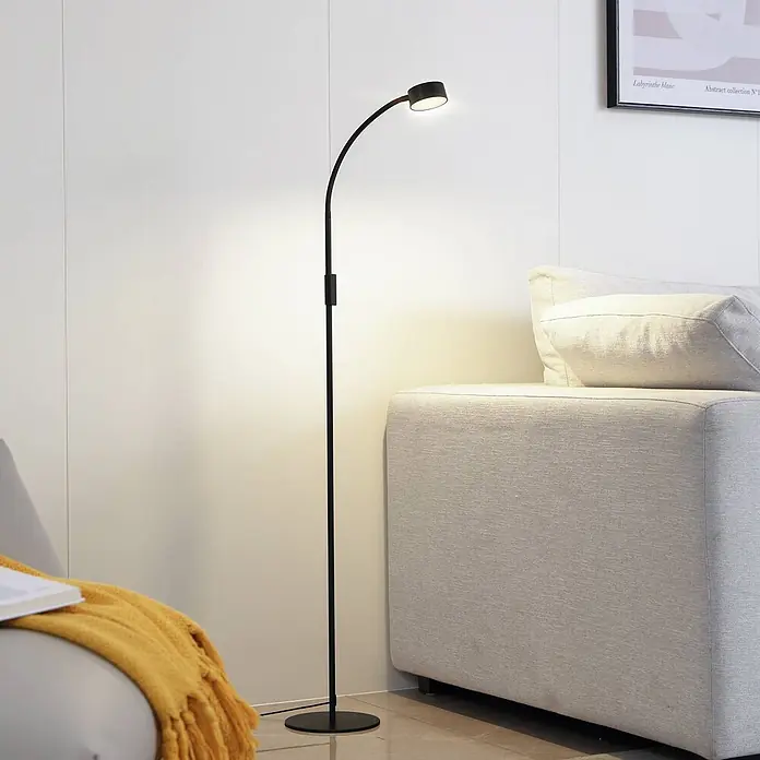 Lindby Stehleuchte Maori - schwarz, schwarz - Moderne schwarze Metall-Stehleuchte mit gebogenem Hals, spendet gerichtetes Licht neben einem hellgrauen Sofa.