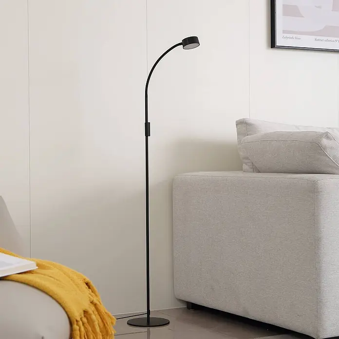 Lindby Stehleuchte Maori - schwarz, schwarz - Schlanke, schwarze Stehlampe mit gebogenem Arm und rundem Kopf, neben einem hellgrauen Sofa.