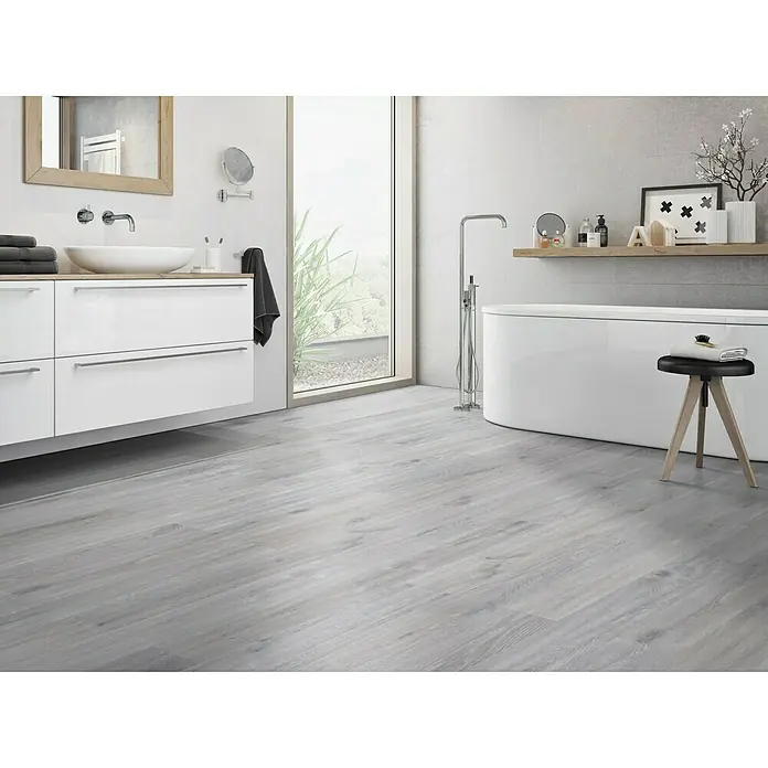 Classen Vinylbodenmuster GreenVinyl Eiche gekalkt Grau - 300 x 173 x 4 mm, Landhausdiele - Badezimmer mit hellem Holzfußboden, weißer Badewanne und Waschtisch. Der Bodenbelag verleiht dem Raum eine moderne und einladende Atmosphäre.