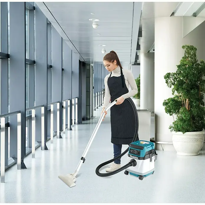 Makita LXT 18V Akku-Nass-Trockensauger DVC150LZ - 36 V, Ohne Akku, Behältervolumen: 15 l - Frau saugt mit einem Makita Akku-Staubsauger einen Flur. Der Staubsauger ist blau-weiß und hat einen flexiblen Schlauch.