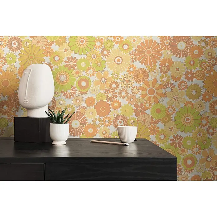 Profhome Vliestapete Heißgeprägte Vliestapete Blumen, Floral, Retro in gelb - creme-weißgrünocker-braun, 8.500 x 530 mm - Lebendige Retro-Blumentapete in Orange, Gelb und Lindgrün, die einen lebhaften Hintergrund für einen dunklen Schreibtisch mit moderner Deko bildet.