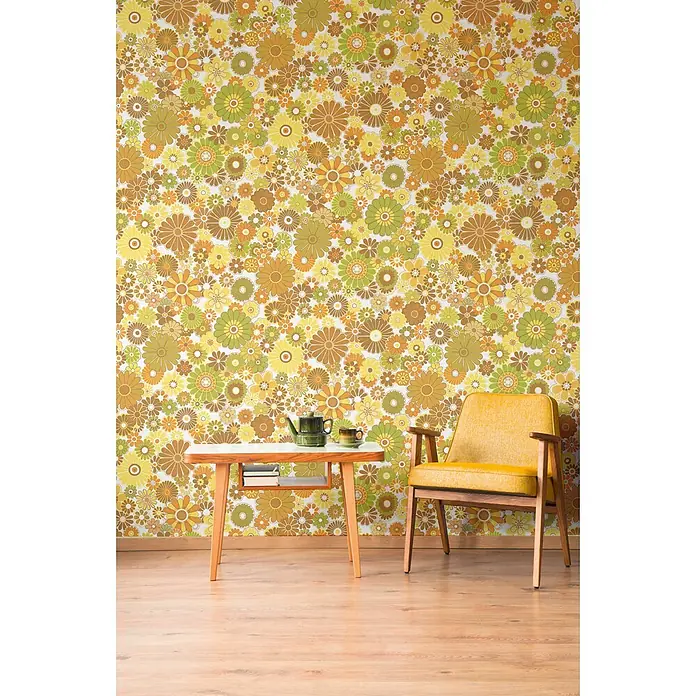 Profhome Vliestapete Heißgeprägte Vliestapete Blumen, Floral, Retro in gelb - creme-weißgrünocker-braun, 8.500 x 530 mm - Ein Retrozimmer mit gelb-brauner Blumentapete, einem Holztisch und einem gelben Sessel.