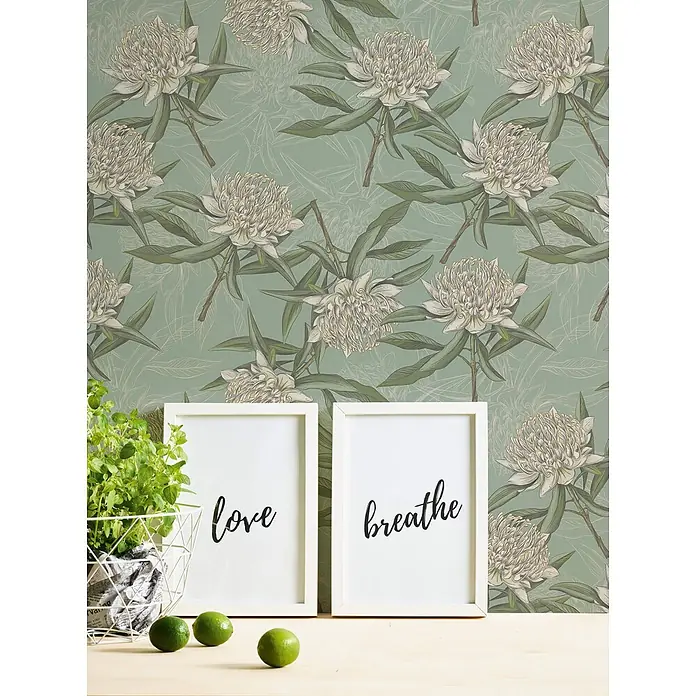 Profhome Vliestapete Vliestapete Blumen, Landhaus, Floral, Romantisch, Natur in blau - grün, 10.050 x 530 mm - Gemusterte Tapete mit großen weißen Blüten und grünen Blättern auf sanftem Grün, ergänzt ein Raumarrangement mit Deko-Rahmen und Pflanze.