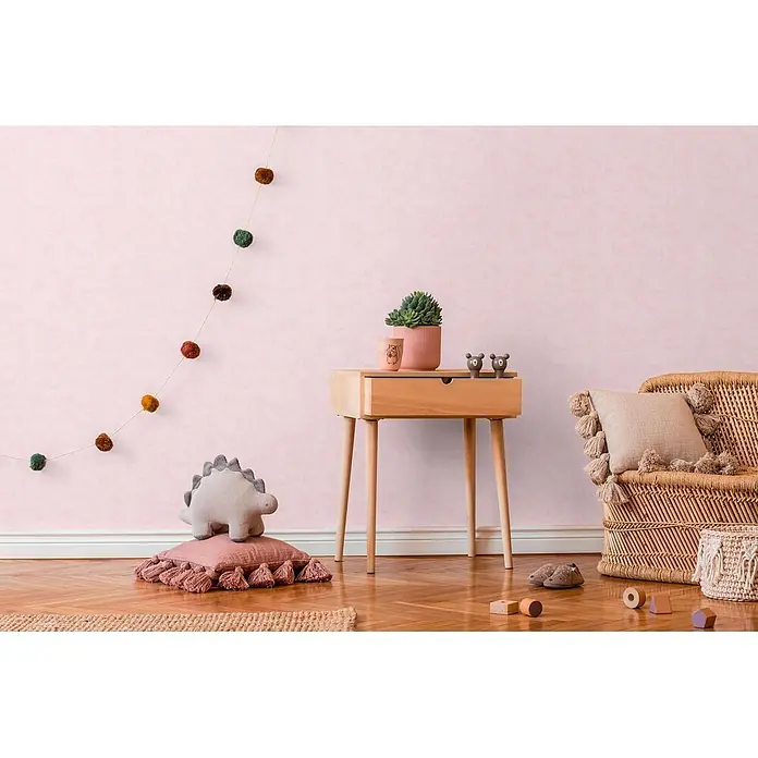 Profhome Vliestapete Vliestapete Kindertapete, Used Look, Textiloptik, Uni in rosa - rosa,lila, 10.050 x 530 mm - Rosa Kinderzimmer mit Holznachttisch, Topfpflanze, Deko, Korbstuhl, Dino-Spielzeug und Pompon-Girlande.