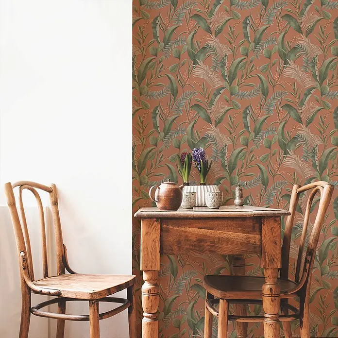 Profhome Vliestapete Vliestapete Blumen, Landhaus, Floral, Romantisch, Palmen, Natur in orange - beigegrünrot, 10.050 x 530 mm - Tapete mit tropischen Blättern auf Terrakotta-Hintergrund an einer Akzentwand, neben weißer Wand und Holzmöbeln.
