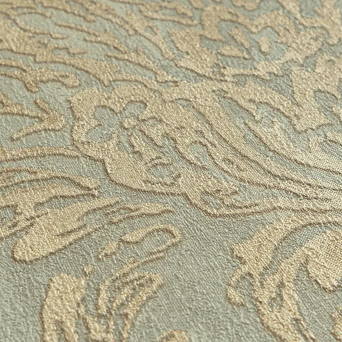 Profhome Vliestapete Heißgeprägte Vliestapete Textiloptik, Ornament, Barock grau - goldgrün-beige, 10.050 x 530 mm - Nahaufnahme von strukturiertem Stoff mit erhabenem, ornamentiertem, hellgoldenem Muster auf blassgrün-grauem Grund.
