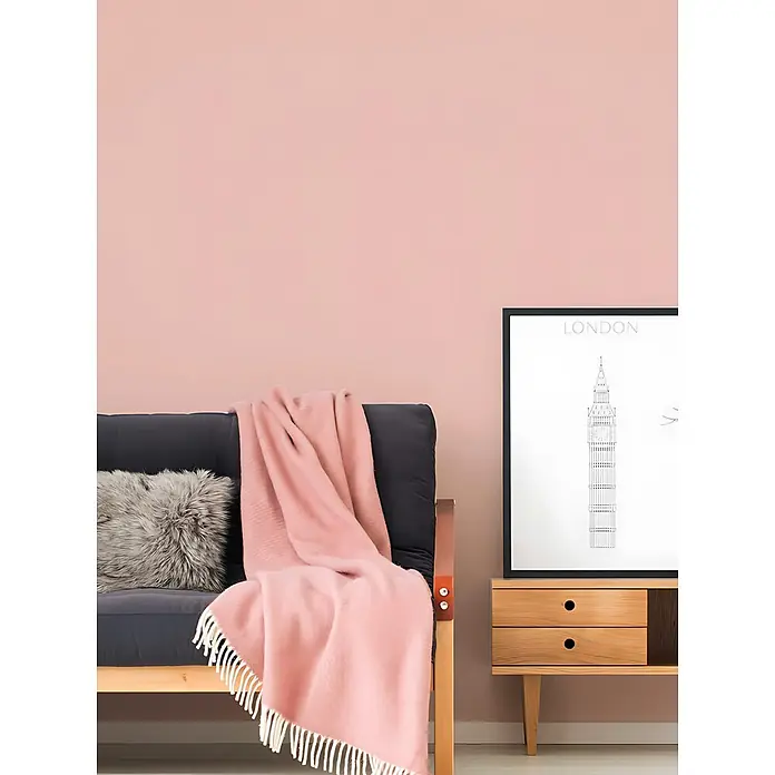 Profhome Vliestapete Vliestapete Uni in rosa - Uni, 10.050 x 530 mm - Ein weicher pinker Überwurf auf einem dunklen Futon mit einem grauen Fellkissen in einem modernen Wohnzimmer.