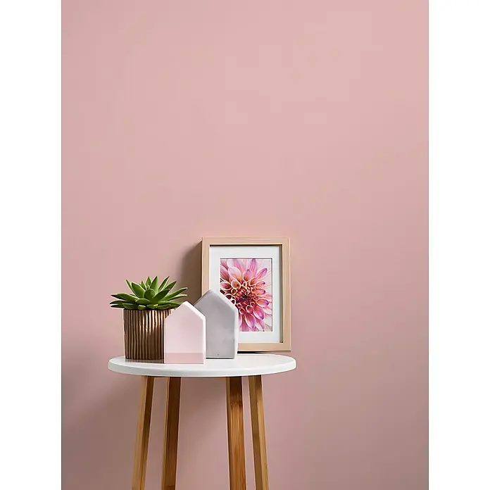 Profhome Vliestapete Vliestapete Uni in rosa - Uni, 10.050 x 530 mm - Weißer runder Beistelltisch mit Holzbeinen, darauf eine Sukkulente, rosa und graue Deko-Häuser und ein gerahmtes Dahlienbild.