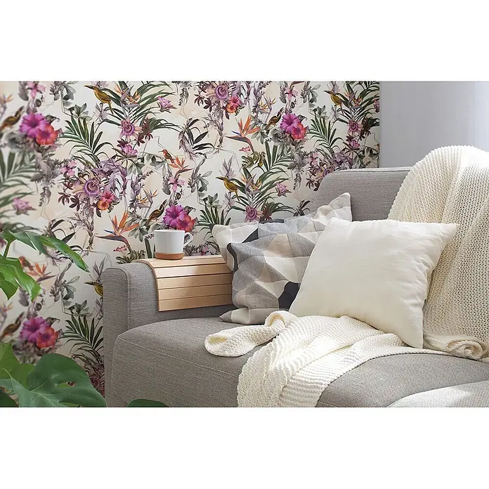 Profhome Vliestapete Glatte Vliestapete ohne Struktur Blumen, Kolibri, Floral in creme - beigegrünrosa, 10.050 x 530 mm - Heller Holzarmlehnen-Organizer mit Lamellen auf grauem Sofa, hält eine weiße Tasse.