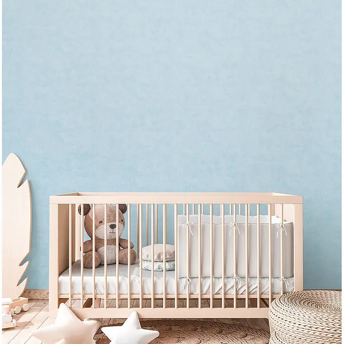 Profhome Vliestapete Vliestapete Kindertapete, Used Look, Textiloptik, Uni in blau - blau-grünhell-blau, 10.050 x 530 mm - Babybett aus hellem Holz mit weißer Bettwäsche und einem Plüschtier darin, in einem gemütlichen Kinderzimmer.