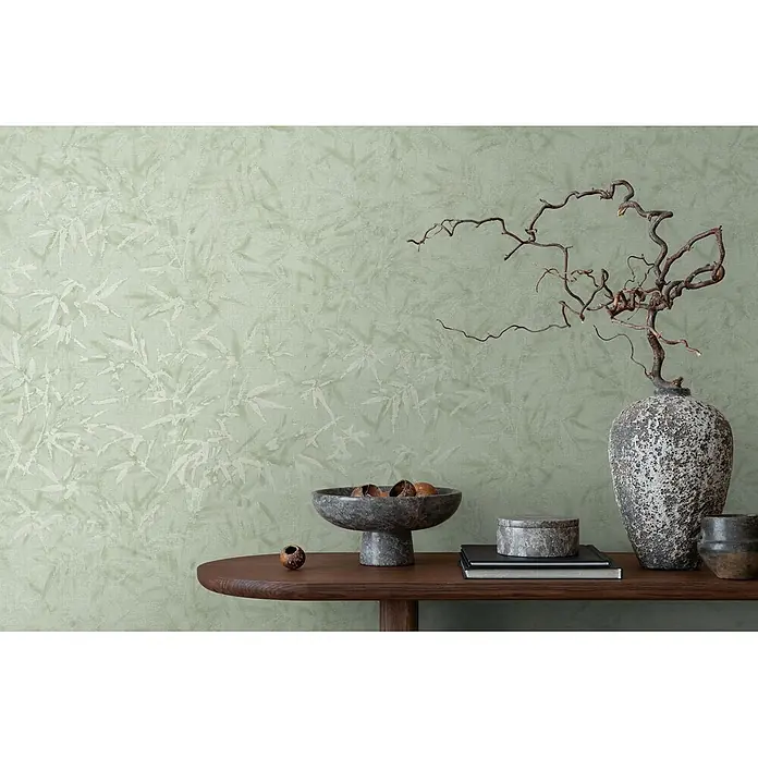 Profhome Vliestapete Heißgeprägte Vliestapete Ton-In-Ton, Floral, Textiloptik in grün - minz-grünsilber, 10.050 x 530 mm - Hellgrüne Tapete mit dezentem Bambusblattmuster, bildet eine ruhige Kulisse hinter einem Holzkonsolentisch mit Dekoartikeln.
