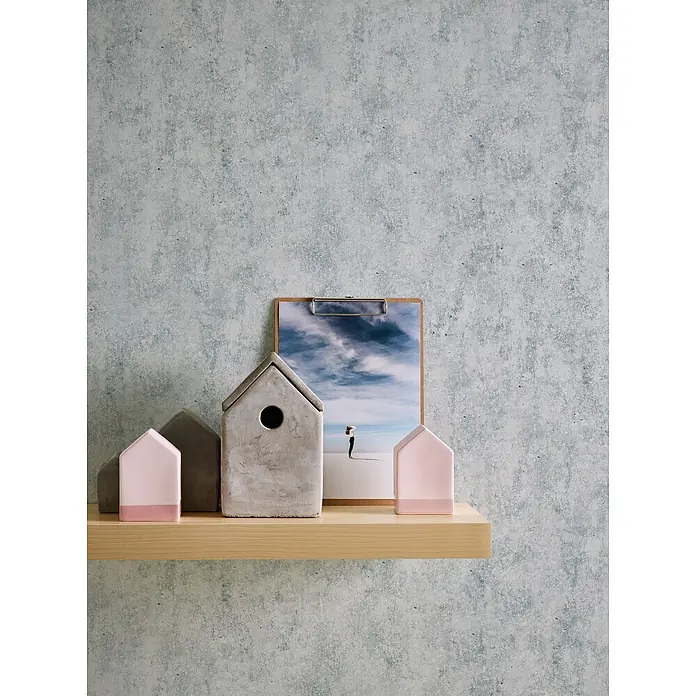 Profhome Vliestapete Vliestapete Steinoptik grau - Steinoptik, 10.050 x 530 mm - Dekorative Beton- und rosa Häuserfiguren auf einem Holzregal, mit einem Bild auf einer Klemmmappe.