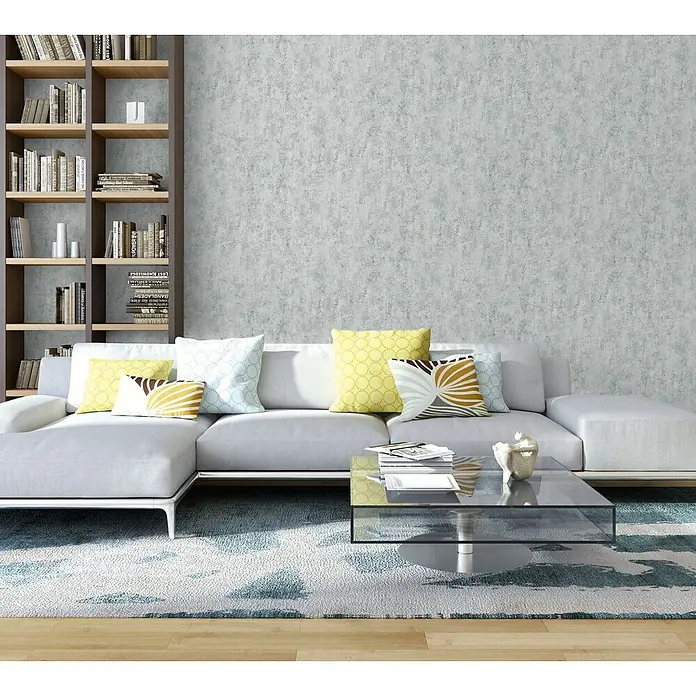 Profhome Vliestapete Vliestapete Steinoptik grau - Steinoptik, 10.050 x 530 mm - Ein modernes Wohnzimmer mit grauem Ecksofa, Glastisch und hohem Bücherregal auf blau-weiß gemustertem Teppich.