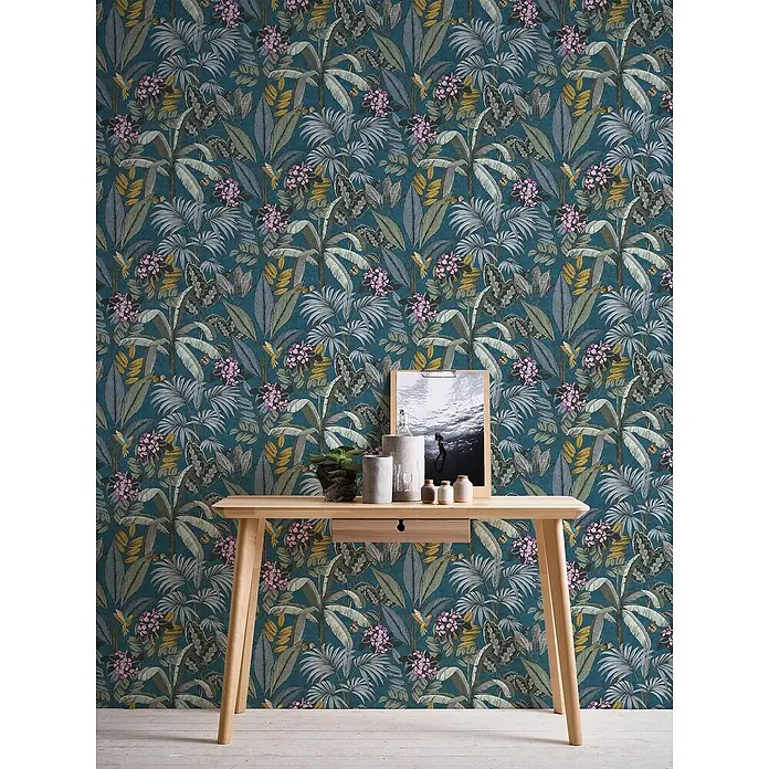 Profhome Vliestapete Glatte Vliestapete ohne Struktur Dschungel in blau - gelbgraugrün, 10.050 x 530 mm - Dunkelblaue Tropen-Tapete mit rosa Blüten und grünen Blättern, passend zu einem hellen Holztisch.