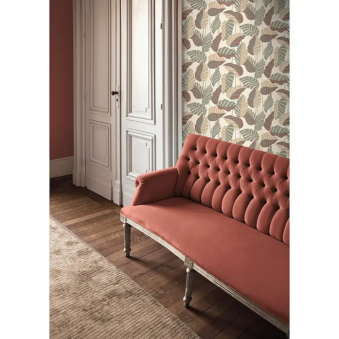Profhome Vliestapete Heißgeprägte Vliestapete Landhaus, Floral, Grafisch beige - creme-weißpatina-grünperl-gold, 10.050 x 530 mm - Getuftetes korallenfarbenes Samtsofa mit geschnitzten Holzbeinen in einem Raum mit gemusterter Tapete.