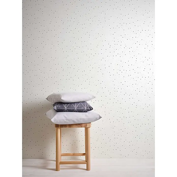 Profhome Vliestapete Vliestapete Kindertapete in blau - grauschwarz, 10.050 x 530 mm - Weiße Tapete mit verstreuten schwarzen Punkten, darauf ein Holzschemel mit gestapelten Kissen.