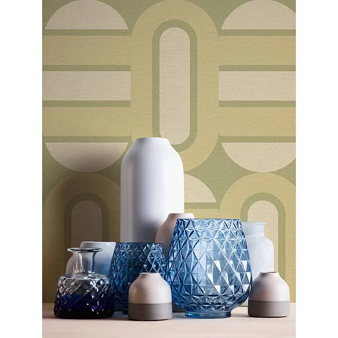 Profhome Vliestapete Heißgeprägte Vliestapete Grafisch, Retro, Geometrisch, Ornament in grün - creme-weißoliv-grün, 8.500 x 530 mm - Eine Sammlung verschiedener Deko-Vasen und Objekte aus weißer Keramik und gemustertem blauem Glas, auf einer Fläche arrangiert.