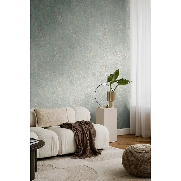 Profhome Vliestapete Heißgeprägte Vliestapete Textiloptik, Ornament, Barock in blau - pastell-türkis, 10.050 x 530 mm - Hellblaue Tapete mit einem verzierten goldenen Damastmuster, die ein gemütliches Wohnzimmer hinter einem cremefarbenen Sofa schmückt.