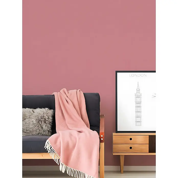 Profhome Vliestapete Vliestapete Uni in rosa - Uni, 10.050 x 530 mm - Ein Wohnzimmer mit rosafarbener Wand, grauem Sofa, weicher rosa Decke und hellem Holzbeistelltisch mit gerahmtem London-Druck.