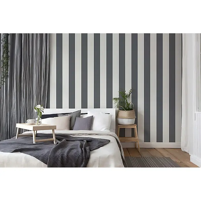 Profhome Vliestapete Vliestapete Traditionell grau - 10.050 x 530 mm - Grau-weiß gestreifte Tapete an einer Schlafzimmerwand hinter einem Bett.