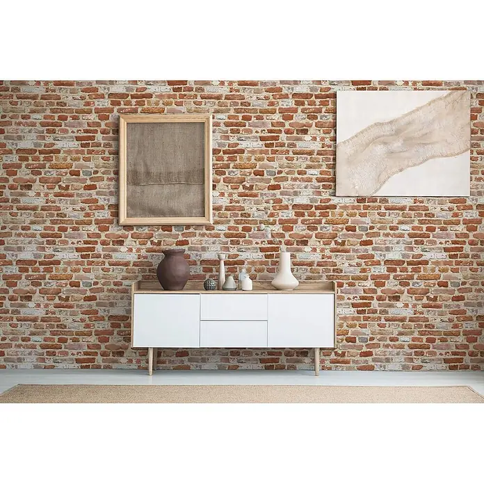 Profhome Vliestapete Heißgeprägte Vliestapete Steinoptik, Ziegelstein, Natur in rot - beigeorange, 10.050 x 530 mm - Ein modernes Sideboard aus weißem und hellem Holz mit zwei Türen und zwei Schubladen, dekoriert mit Vasen und Bildern, vor einer Ziegelwand.