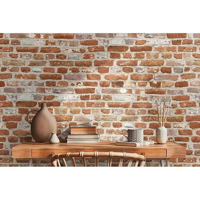 Profhome Vliestapete Heißgeprägte Vliestapete Steinoptik, Ziegelstein, Natur in rot - beigeorange, 10.050 x 530 mm - Rustikale rote Ziegelwand mit weißem Mörtel, hinter einem Holzschreibtisch mit Dekoartikeln.
