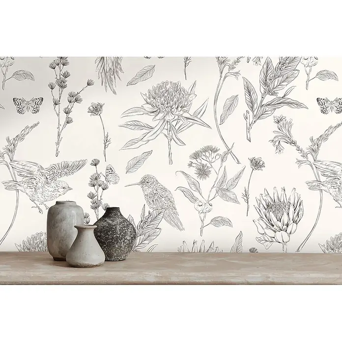Profhome Vliestapete Vliestapete Blumen, Landhaus, Floral, Toile De Jouy, Vogelmuster, weiß - schwarz, 10.050 x 530 mm - Schwarz-weiße botanische und Vogel-Tapete hinter drei Keramikvasen auf einem Holztisch.