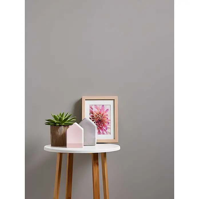 Profhome Vliestapete Vliestapete Uni grau - Uni, 10.050 x 530 mm - Eine Sukkulente in einem gerippten Topf, rosa und graue Hausdekorationen und ein gerahmtes Dahlienbild auf einem weiß gedeckten Holztisch.