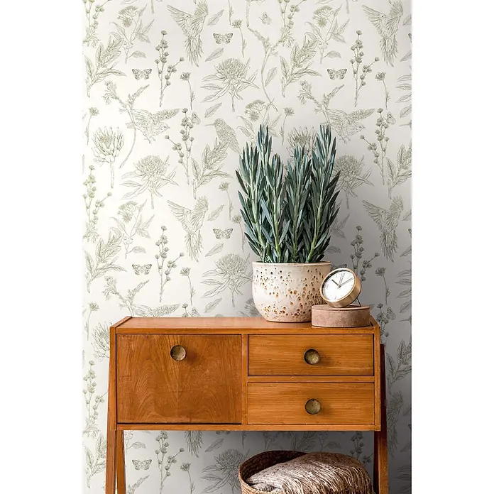 Profhome Vliestapete Vliestapete Blumen, Landhaus, Floral, Toile De Jouy, Vogelmuster, weiß - grün, 10.050 x 530 mm - Holznebentisch mit zwei Schubladen und einem Schrank, der eine Topfpflanze und eine Uhr vor gemusterter botanischer Tapete hält.
