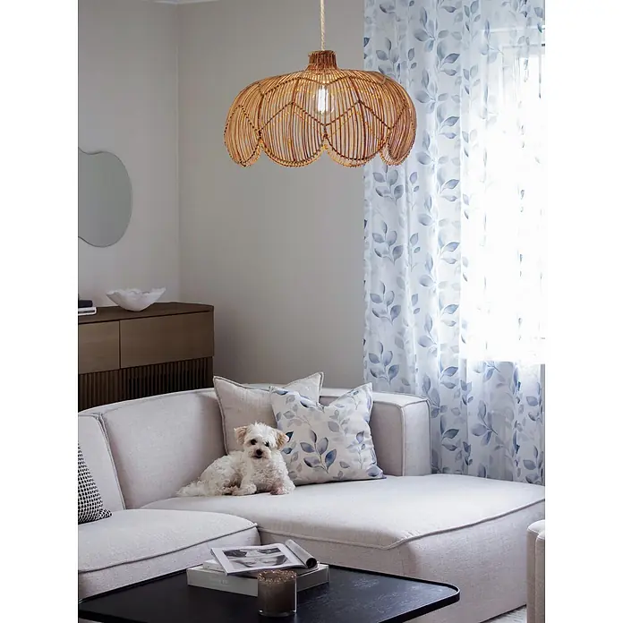 PR Home Pendelleuchte Belle - 40 W, E27 - Geflochtene Rattan-Pendelleuchte beleuchtet ein modernes Wohnzimmer mit hellem Sofa, gemusterten Vorhängen und einem kleinen Hund.