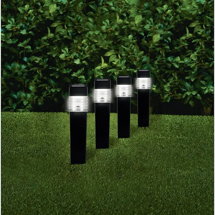BAUHAUS Solarleuchten-Set Piazza - 4 Stk., L x B x H: 6 x 6 x 39 cm, Anthrazit, IP44, 3 lm - Reihe von schwarzen Solar-Gartenleuchten mit weißem Lampenschirm auf einem Rasen vor einer Hecke, die den Gartenweg beleuchten.