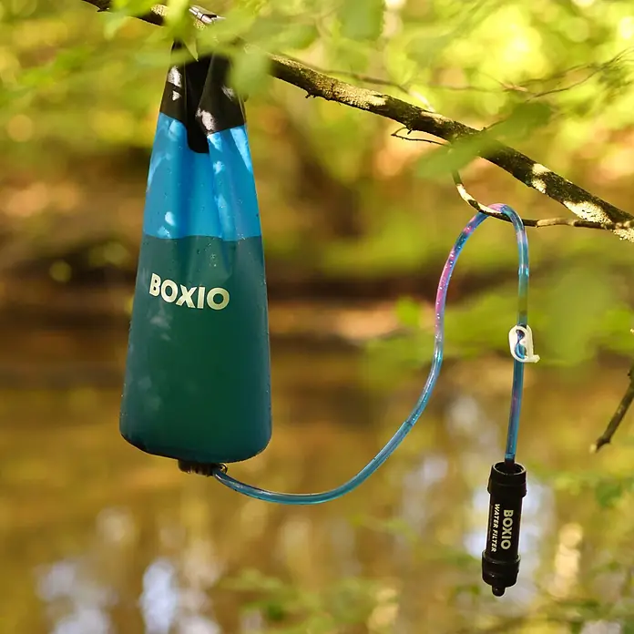 Boxio Campingwaschbecken Wash Max+ - 40 x 30 x 40 cm, 5 -tlg. - BOXIO Wasserfiltersystem, blaue Tasche und schwarzer Filter, hängt draußen an einem Ast.