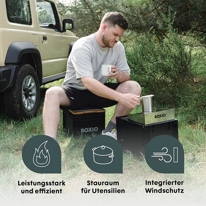 Boxio Gaskocher Cook Plus - 40 x 30 x 27 cm, Edelstahl - Mann nutzt ein schwarzes BOXIO Campingküchensystem mit schwarzen Kisten und einer Metallkochereinheit, draußen neben einem SUV.