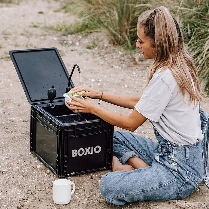 Boxio Campingwaschbecken Wash - 40 x 30 x 28 cm, 1 -tlg. - Schwarze Boxio Outdoor-Waschstation, von einer Frau zum Abwaschen einer Tasse genutzt.