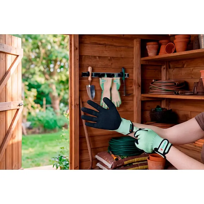 Gardol Gartenhandschuhe für Pflanzarbeiten - 9, L, Grün, 1 Stk. - Eine Person zieht hellgrüne und schwarze Gartenhandschuhe in einem Gartenschuppen an.