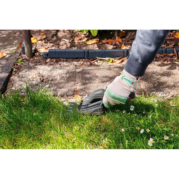 Gardol Gartenhandschuhe für den Geräteeinsatz - 8, M, Mint - Eine behandschuhte Hand verwendet einen grau-schwarzen Hand-Rasentrimmer zum Schneiden von Gras am Betonweg.