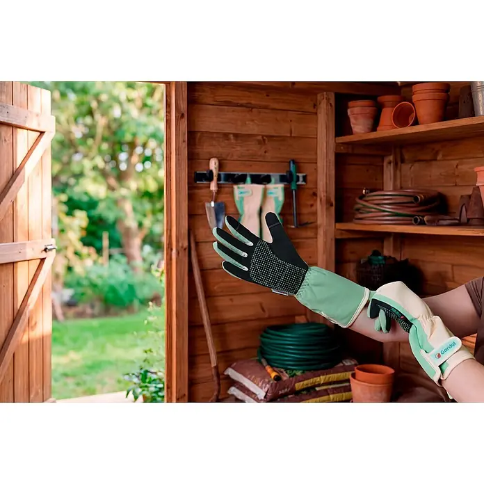 Gardol Gartenhandschuhe mit Stulpen - 8, M, Mint - Person zieht lange hellgrüne und schwarze Gartenhandschuhe in einem Schuppen an.