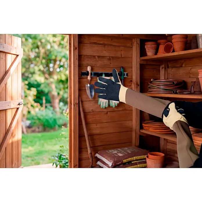 Gardol Gartenhandschuhe - 8, M, Braun - Person zieht langärmlige Gartenhandschuhe mit schwarzen Handflächen und braunen Ärmeln in einem Gartenhaus an.