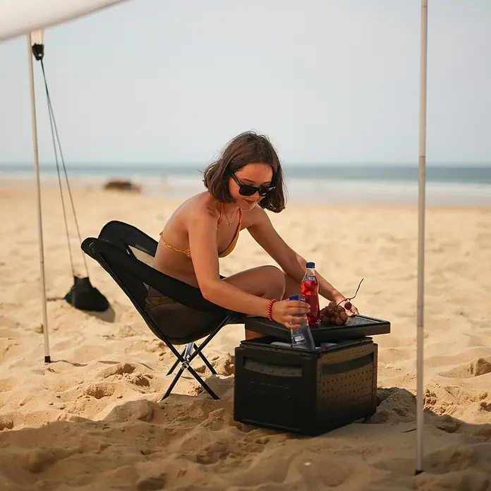 Boxio Kühlbox Cool Plus - Schwarz, 16 l, 3 -tlg. - Schwarze BOXIO Kühlbox am Strand, von einer Person zur Aufbewahrung von Getränken und Snacks genutzt.