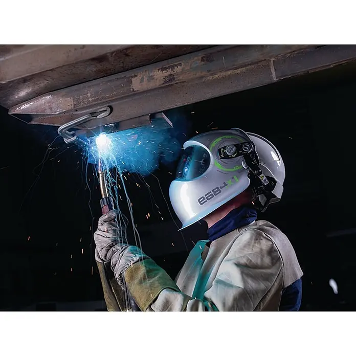 Optrel Schweißhelm E684 -  - Weißer Schweißhelm mit grünen Akzenten, getragen von einer Person beim Schweißen, Lichtbogen und Funken sichtbar.