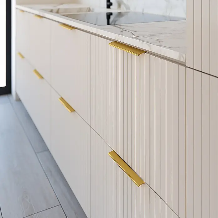 Cordia Möbelgriff 10 cm - Lochabstand: 60 mm, Aluminium, Gold - Nahaufnahme moderner, hellbeiger Küchenschränke und -schubladen mit vertikaler Riffelung, eleganten goldenen Griffen und weißer Marmor-Arbeitsplatte.