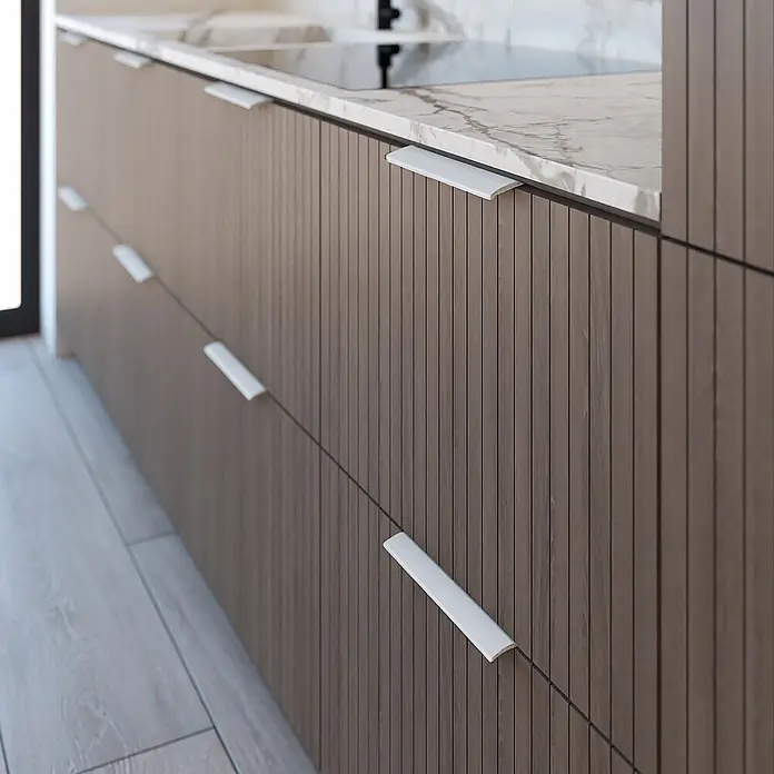 Cordia Möbelgriff 12 cm - Lochabstand: 96 mm, Aluminium, Weiß - Weiße Griffleisten an braunen, gerillten Küchenschränken unter einer Marmorarbeitsplatte.