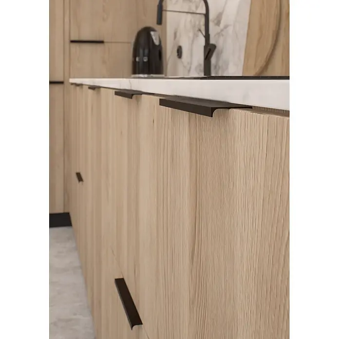 Cordia Möbelgriff 12 cm - Lochabstand: 96 mm, Aluminium, Schwarz - Schwarze, integrierte Griffe an hellen Holzküchenschränken mit weißer Arbeitsplatte.