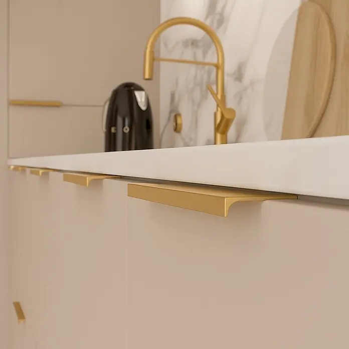 Cordia Möbelgriff 30 cm - Lochabstand: 260 mm, Aluminium, Gold - Mattgoldener Kanten-Schrankgriff unter einer weißen Arbeitsplatte an beigefarbenen Küchenschränken.