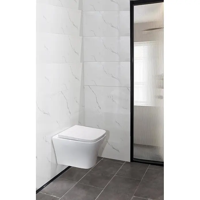 Sanicomfort Wand-WC-Set Artio - Spülrandlos, Spülform: Tief, WC Abgang: Waagerecht, Weiß - Weißes wandhängendes WC in einem modernen Badezimmer mit weißen Marmoroptik-Wänden und dunklem Boden, neben einer gerillten Glastrennwand.
