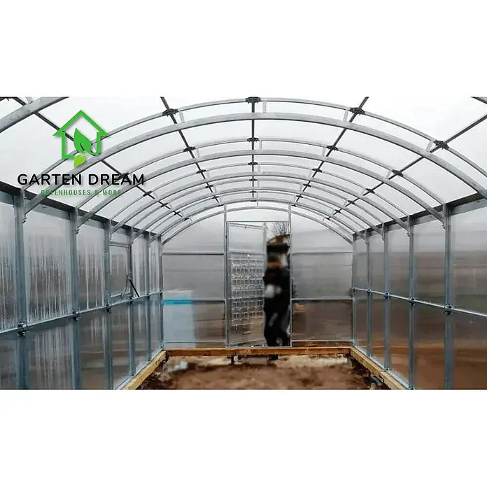 Garten Dream Gewächshaus Gardener, 4mm Polycarbonat - Außenmaß inkl. Dachüberstand (B x T): 300 x 600 cm, Material Seitenwand: Kunststoff, 4 mm, Silber - Geräumiges Gewächshaus-Interieur mit gewölbtem Metallrahmen und klaren Polycarbonatplatten, zeigt Eingang und Erdboden.