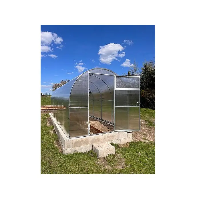 Garten Dream Gewächshaus Mini, 4mm Polycarbonat - Außenmaß inkl. Dachüberstand (B x T): 200 x 600 cm, Material Seitenwand: Kunststoff, 4 mm, Silber - Gewölbtes Gewächshaus mit transparenten Paneelen und Metallrahmen, auf Betonfundament im Gras, Tür offen.
