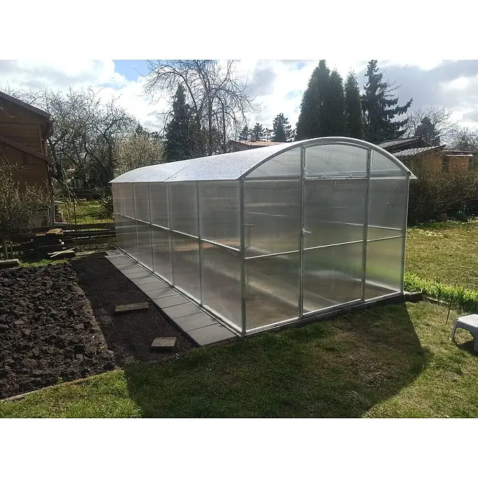 Garten Dream Gewächshaus Gabriela, 6mm Polycarbonat - 300 x 600 cm, 6 mm, Silber - Gewölbtes Polycarbonat-Gewächshaus mit Aluminiumrahmen in einem Garten, neben einem frisch umgegrabenen Beet.