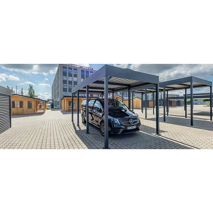 Carport Planer - Konfigurierbar, Stahl - Ein anthrazitfarbener Metall-Carport schützt einen schwarzen Mercedes-Van auf einem gepflasterten Parkplatz, mit ähnlichen Carports und Holzhütten in der Nähe.